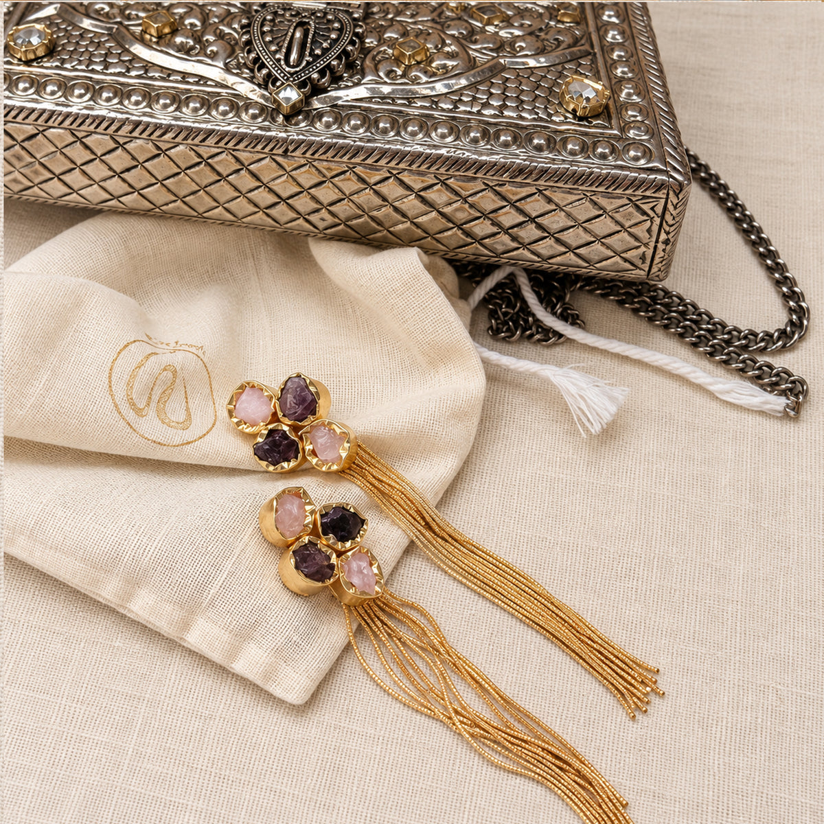 Fiora natural stone tassel earrings styled beside an ornate silver clutch